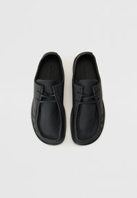 Fekete bőrcipők lekerekített dizájnnal, varrott részletekkel és texturált béléssel a tapadás érdekében. Slip-on stílus, fűzők nélkül.