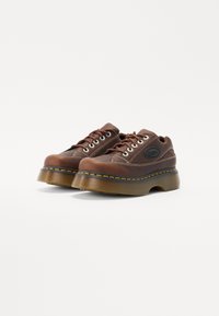 Scarpe con plateau marroni con una tomaia in pelle texturizzata, dotate di occhielli in metallo, cuciture a contrasto e una soletta spessa in gomma trasparente.