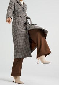 Grå rutig lång kappa med bälte, i kombination med bruna vida byxor och beige spetsiga klackar. Texturerad tyg och skräddarsydd design.