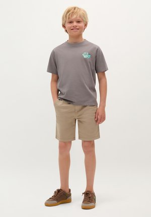 Graues T-Shirt mit Handdruck-Detail, beige Shorts und braunen Sneakers mit grünen Akzenten. Lässige Passform, schlichte Texturen, einfaches Design.