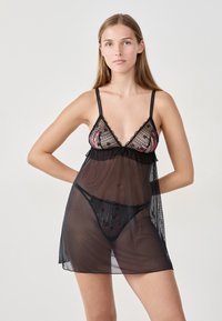Lingerie nera in rete con ricami floreali, bordo ondulato, spalline sottili e una texture trasparente. Include un perizoma nero abbinato.