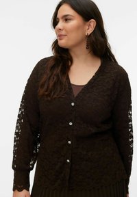 Črni čipkasti kardigan z dolgimi rokavi, V-izrezom in dekorativnimi gumbi. Ima cvetlični vzorec in valovit rob. Nošen čez temnejšo majico.