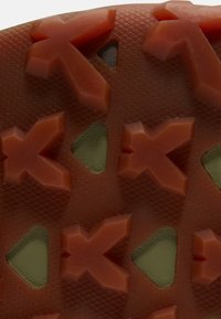 Disegno del battistrada con tacchetti in gomma arancione a forma di freccia sporgenti e aree verdi triangolari incassate sulla superficie della suola testurizzata.