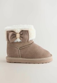 Tan suède laars met een zachte witte bontmanchet en een grote bruine strikaccent. Beschikt over een rubberen zool en stiksels langs de naden.
