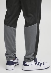 Sorte og grå joggebukser med et strømlinjeformet design og glatt tekstur, kombinert med hvite og marineblå sneakers med tre striper.