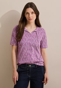Blusa morada de manga corta con un estampado de hojas, que cuenta con un cuello con muesca y una tela suave. Combinada con pantalones de mezclilla azul oscuro.