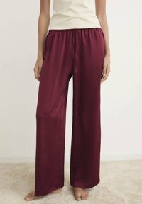 Pantaloni a palazzo in satin bordeaux con vita elastica e cordoncino, caratterizzati da una superficie liscia e una vestibilità ampia.
