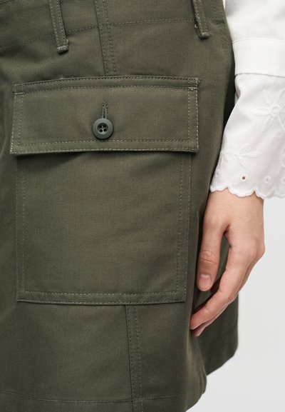 Χακί cargo σορτς με μεγάλη τσέπη-μπαλωτή, κλείσιμο με κουμπί και εμφανείς ραφές. Το ύφασμα έχει λεία, ανθεκτική υφή.