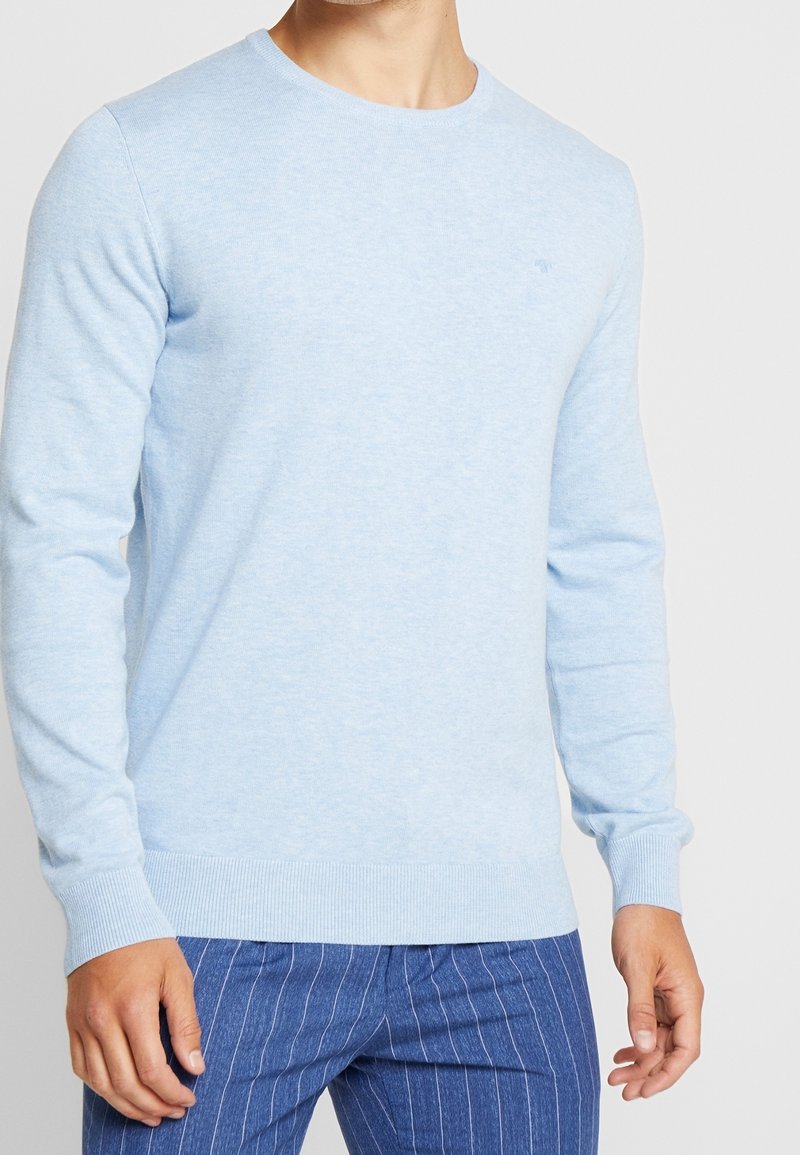 Light blue sweater made of soft material, featuring a round neckline and long sleeves. Ribbed cuffs and hem. Casual design paired with striped pants.
