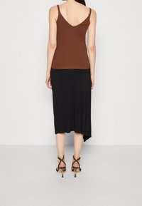 Brown fitted tank top with adjustable straps paired with a black asymmetrical skirt, complemented by strappy black heels. Smooth textures.