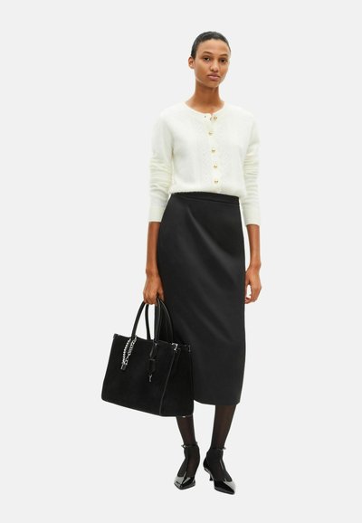 Cremefarvet kabelstrikket cardigan med guldknapper, sort pencilnederdel, sort ruskindshåndtaske med kædeaccent og spidse sorte hæle.