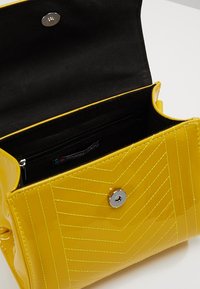 Borsa a mano in pelle sintetica gialla con motivo a chevron trapuntato, chiusura a scatto argentata e foderatura in tessuto nero con tasca con zip.