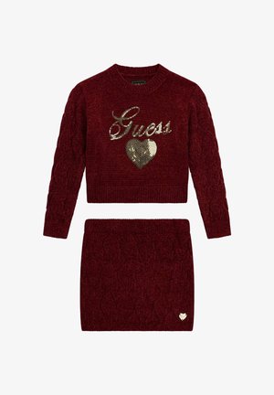 Rotes Strickset aus Pullover und passendem Rock mit Zopfmuster, goldfarbenem Pailletten-Logo "Guess" und Herzapplikation am Rock.