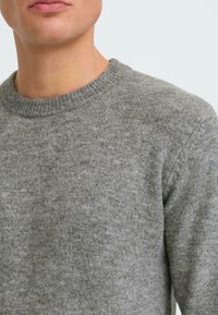 Jersey de punto gris con escote redondeado, que presenta una textura suave y un ajuste clásico. Enfoque en los detalles de la tela y las costuras.