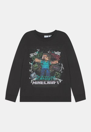 Felpa nera con design grafico di un personaggio squadrato contro un muro di mattoni. Elementi di testo e accenti colorati migliorano l'attrattiva visiva.