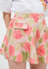 Gonna a fantasia floreale con tonalità rosa e verde, texture leggera, design plissettato e tasche laterali. Elegante, lunghezza a metà coscia.