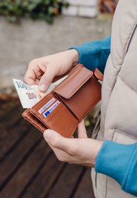 Brown leather wallet with a snap closure, holding banknotes and multiple card slots, displayed in a hand against a neutral background.
