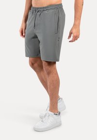 Grijze sportshorts met een elastische tailleband, een trekkoord en zijzakken. Gepaard met witte sneakers.