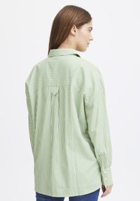 Green and white striped button-up shirt with a back yoke, long sleeves, and cuff buttons, displayed on a model from the back.