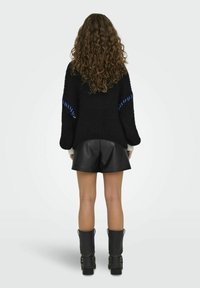 Suéter de punto negro con acentos azules en las mangas, combinado con pantalones cortos de cuero negros y botas negras hasta la rodilla. Cabello rizado visible.