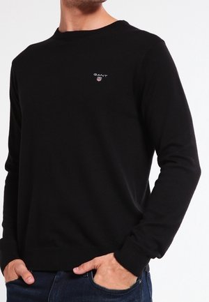 Maglione nero a maniche lunghe realizzato in tessuto morbido, con scollo rotondo e un piccolo logo ricamato sul lato sinistro del petto.