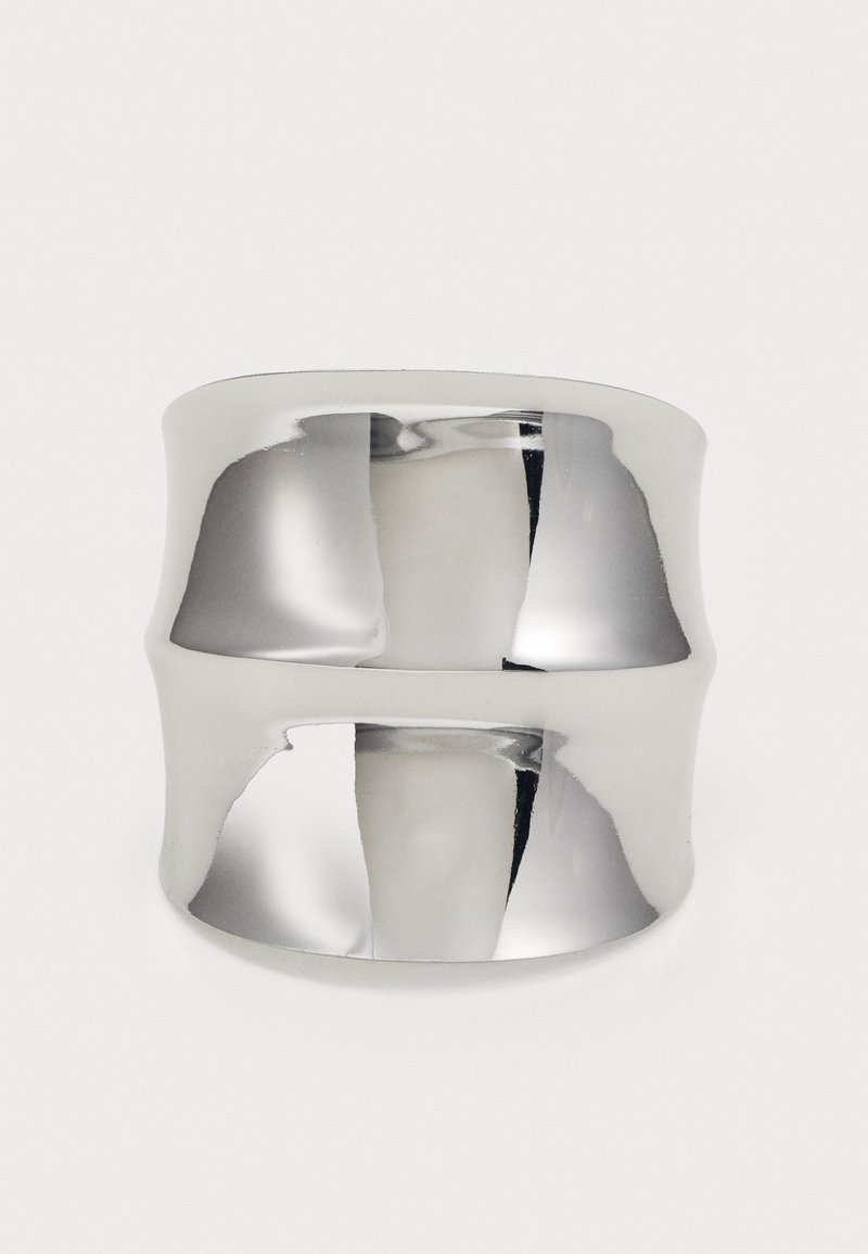 Zilveren manchet ring met een gladde, reflecterende oppervlakte. Heeft een gebogen ontwerp en brede band, wat zorgt voor een moderne, minimalistische uitstraling.