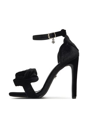 Czarna aksamitna sandałka na wysokim obcasie z paskiem wokół kostki, kwiatowym detalem na palcach i smukłym obcasem typu szpilka. Teksturowany materiał, elegancki design.