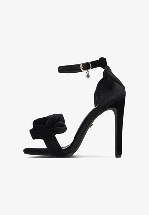 Mustast sametist kõrge kontsaga sandaal, millel on pahkluu rihm, lilleline detail varbal ja elegantne stilettokonts. Tekstuuriga materjal, peen disain.