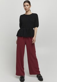 Sort tekstureret peplum top med korte ærmer, parret med løse bordeaux bukser. Looket afsluttes med kraftige sorte sko.