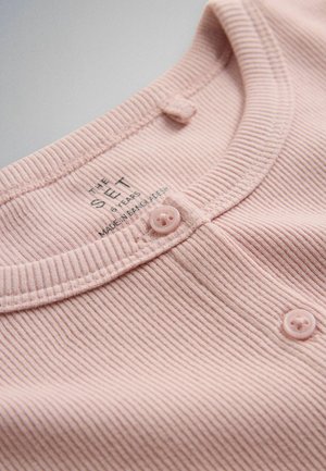 Vaaleanpunainen, poimutettu kankainen yläosa, jossa pyöreä pääntie ja kaksi nappia, kokoetiketti kertoo "6 vuotta" ja "Valmistettu Bangladeshissa".