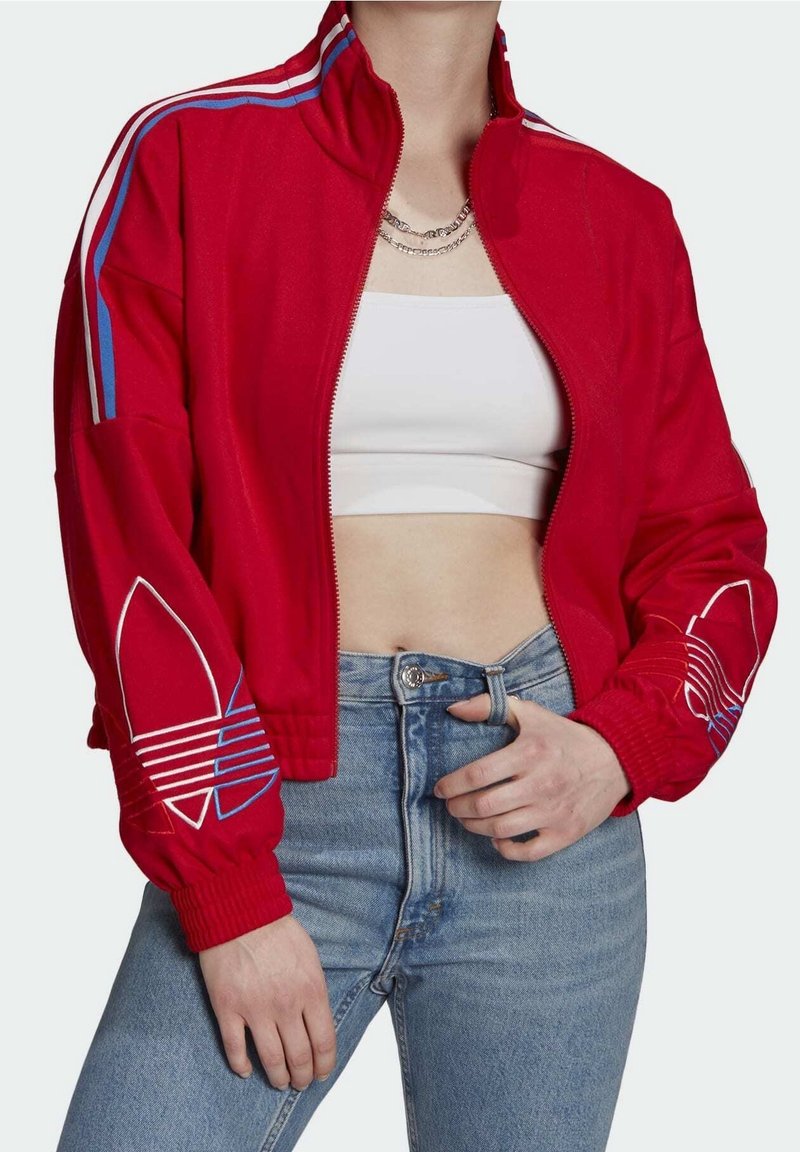 Rode zip-up jas van zacht materiaal, met blauwe en witte strepen over de schouders en logo-ontwerpen op de mouwen; aansluitend ontwerp.