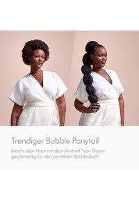 Frau im weißen Kleid mit natürlichem Afro-Haar und gestyltem Bubble-Ponytail, die den Ponytail hält, vor einem neutralen beigen Hintergrund.