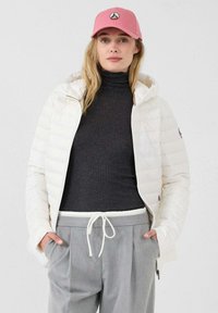 Giacca imbottita bianca con cappuccio, dolcevita grigio e pantaloni grigio chiaro con coulisse. Cappellino rosa con dettaglio logo.