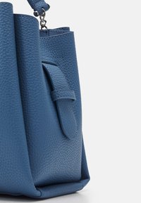 Modrá kožená kabelka s texturovaným povrchem, která má přední kapsu a strukturovaný design. Obsahuje krátké ucho a kovové akcenty.