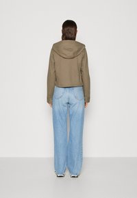 Olivgrön kort jacka med huva, tillverkad av bomull, och långa ärmar. Kombinerad med ljusblå vida jeans.