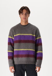 Szürke gyapjú pulóver vízszintes csíkokkal lila, piros és sárga színben. Kerek nyakkivágással és bordázott mandzsettákkal rendelkezik, puha tapintású.