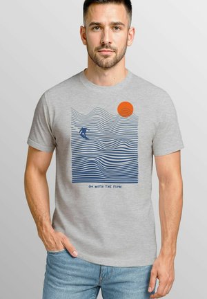 Gray t-shirt featuring a blue wave design with a surfer and an orange sun. Text reads "Go with the Flow" at the bottom.