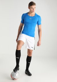 Niebieska sportowa koszulka Puma, białe szorty, czarne skarpetki do kolan i czarne korki. Posiada logo na klatce piersiowej i boku szortów.