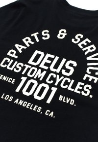 Black cotton t-shirt featuring large white text that reads "PARTS & SERVICE," "DEUS CUSTOM CYCLES," and "1001 BLVD. LOS ANGELES, CA."