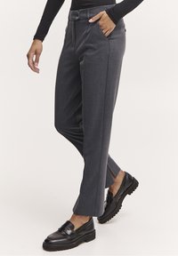 Grå skräddarsydda byxor med smal passform, utrustade med bälteshällor, sidofickor och en delad fålldesign, kombinerat med svarta loafers.