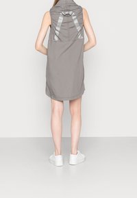 Vestido gris sin mangas con un cuello alto, que presenta un diseño de espalda fruncida y detalles en cinta de satén, combinado con zapatillas blancas.