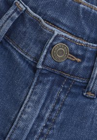 Jeans i denim med mörkblå färg, som har en metallknappstängning, kontrasterande beige stickning och en subtilt sliten textur.