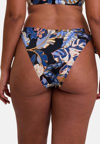 Bas de bikini taille haute en tissu extensible, orné d'un motif floral éclatant sur un fond marine, avec une coupe coquine et des liens sur les côtés.
