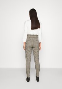 Rutig högmidjade byxor i svart och vitt med en åtsittande design. Har bakfickor och midjebälte. Bärs med en vit topp.