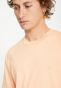 Peachfarvet t-shirt med rund hals og korte ærmer. Har et lille broderet logo på brystet. Blødt, let stof.