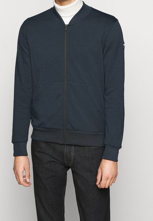 Marineblauwe sweatervest met ritssluiting, een geribbelde kraag, twee zakken aan de voorkant en contrasterende manchetten. Gemaakt van zachte stof met een gladde textuur.