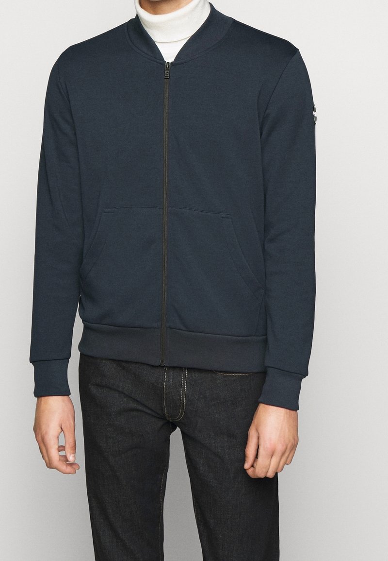 Felpa blu navy con zip, colletto a coste, due tasche frontali e polsini a contrasto. Realizzata in tessuto morbido con una texture liscia.