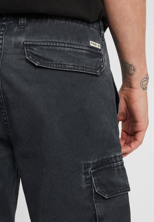 Pantaloni cargo grigio scuro in misto cotone, dotati di molteplici tasche e una finitura testurizzata. Include un piccolo etichetta sulla tasca posteriore.