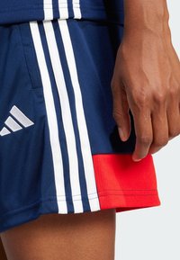 Marine sportshorts met witte strepen en rode accenten. Gemaakt van gladde stof, voorzien van een Adidas-logo en een verstelbare taille.