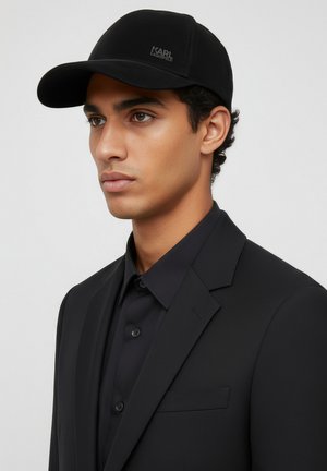 Cappellino da baseball nero con un design strutturato e logo, abbinato a un completo e camicia nere, caratterizzato da una vestibilità slim e una tasca singola sul petto.